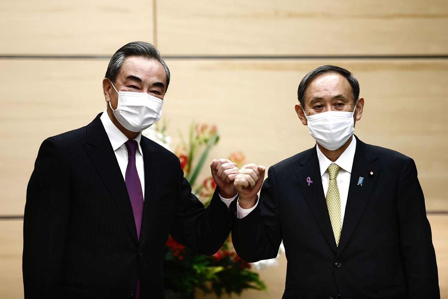 由于新冠肺炎疫情，王毅和菅义伟会晤时，两人都戴着口罩。（Reuters）
