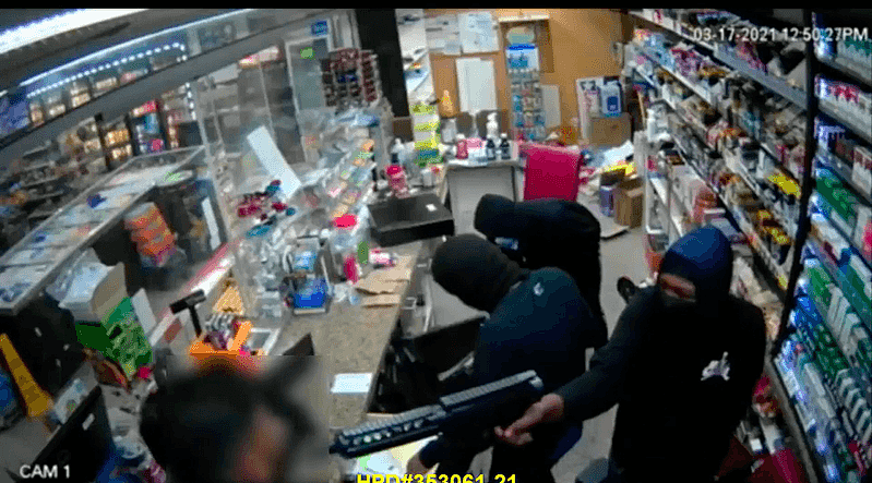 抢匪持长枪抵住店员的脸，让店员打开收银机，视频显示他们抢走了钱和几条香烟。 （警方视频截图）