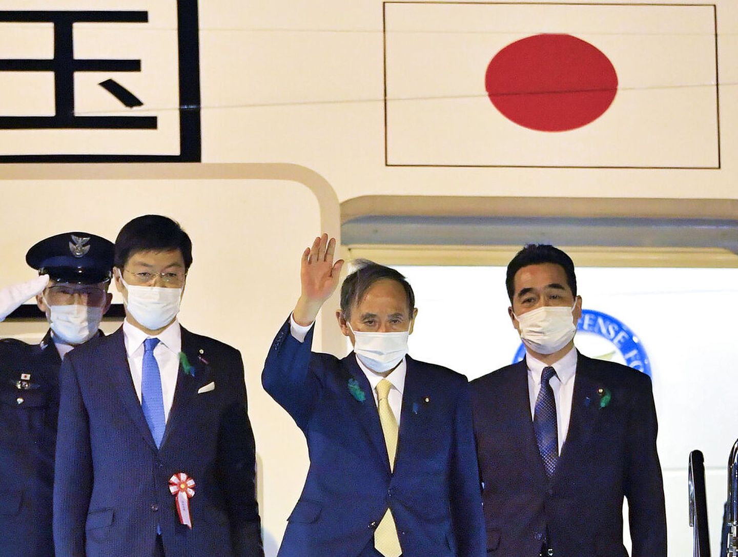 2021年4月15日，日本首相菅义伟（中）在东京羽田机场挥手，准备前往美国进行访问。（AP）
