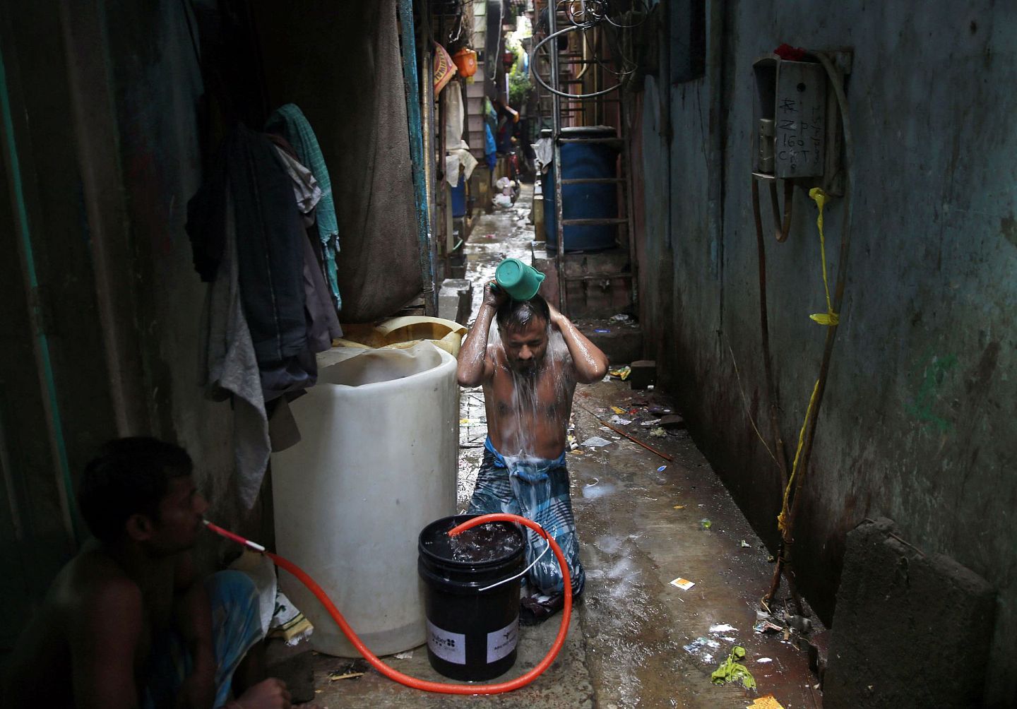 在孟买达拉维贫民窟，一名男子在房子外面洗澡，该地区坐落在繁忙的火车轨道和污染严重的密西河之间，附近是狭窄的小巷子，许多人居住在锡棚里，几乎没有私人浴室，卫生条件极差。（AP）