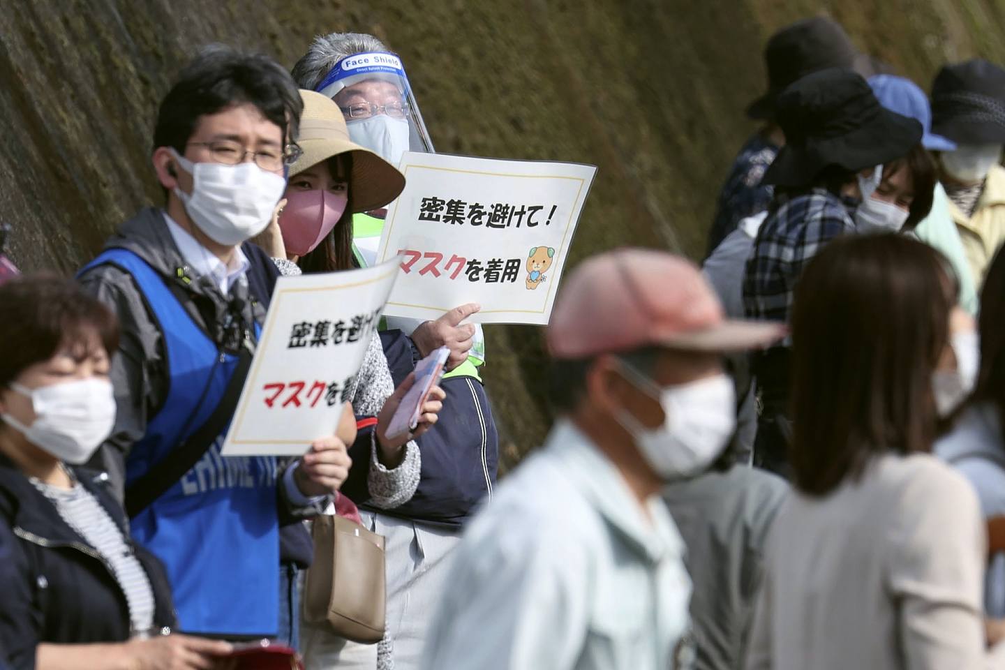 图为2021年4月22日，日本爱媛县砥部町举行东京奥运圣火传递期间，有工作人员举起指示提醒人避免聚集和要戴口罩。 （美联社）