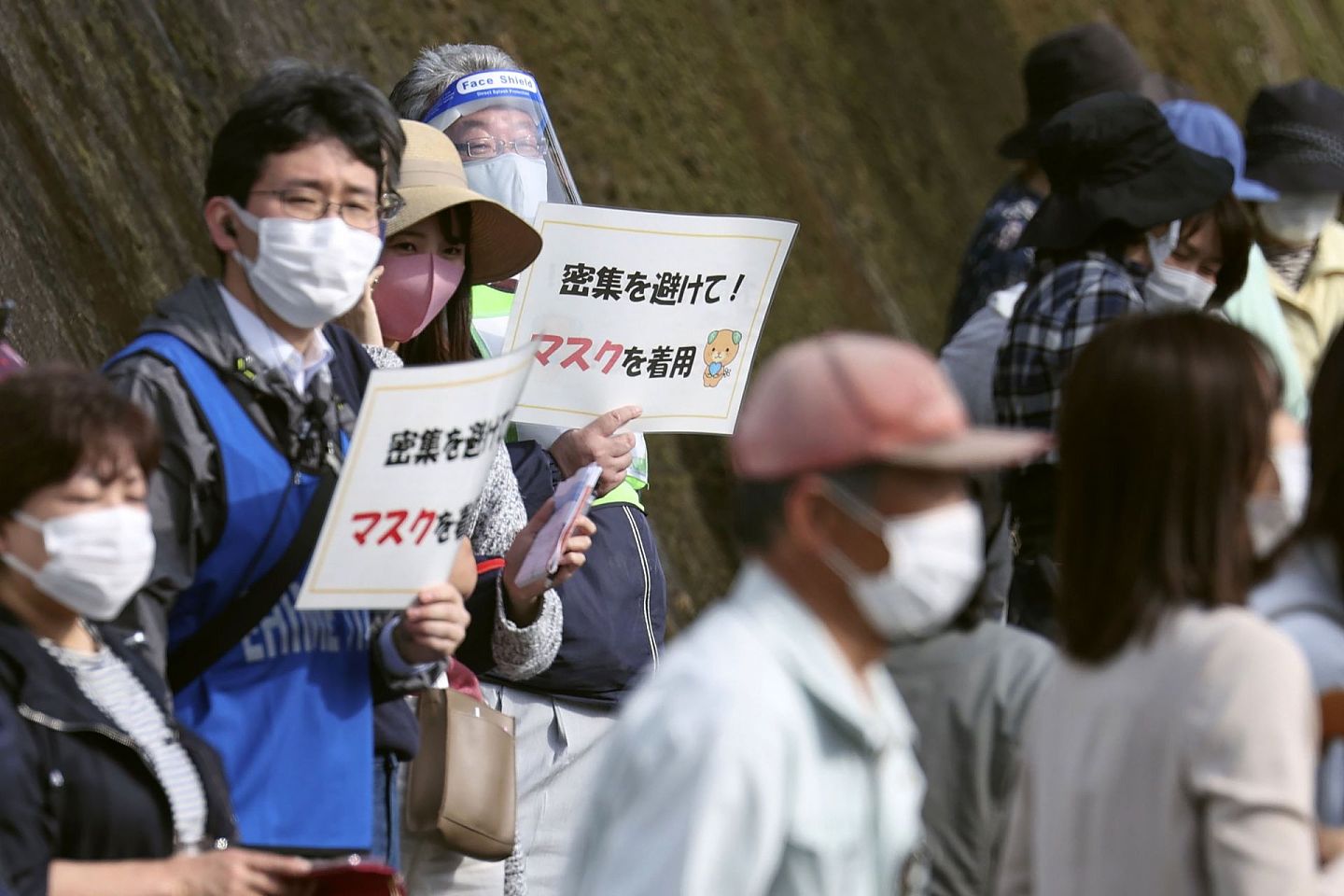 4月22日，日本爱媛县砥部町举行东京奥运火炬传递期间，工作人员举着标志牌，提醒人们避免聚集和要佩戴口罩。（AP）
