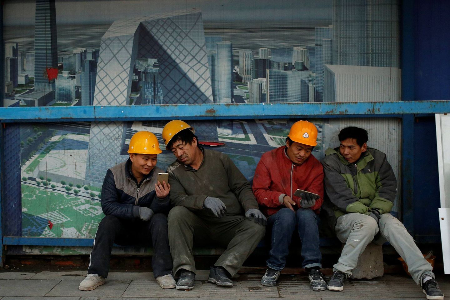 户籍制度松动后进城务工，改变了无数中国农民的命运。图为北京的农民工坐在建筑工地外看手机。（Reuters）