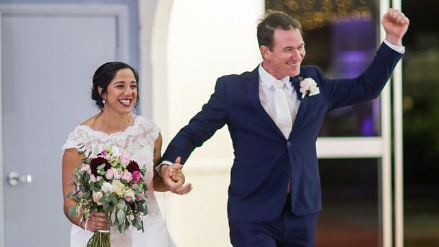 Melissa and Mez enter room holding hands, with Mez fist-pumping the air