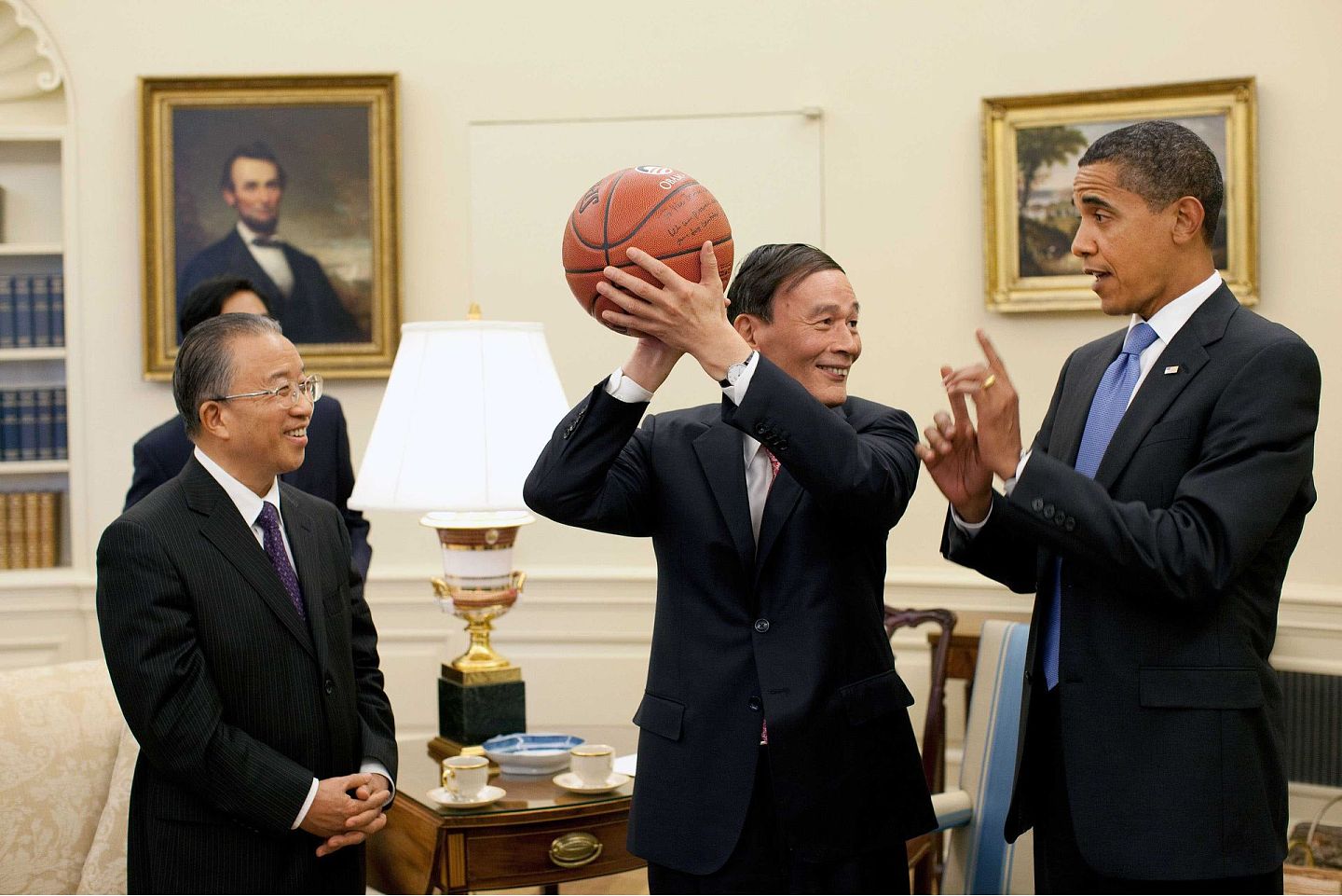 2009年7月28日，时任美国总统奥巴马（右）在白宫会见正在华盛顿出席首轮中美战略与经济对话的时任国务院副总理王岐山（中）和国务委员戴秉国一行。这是奥巴马向王岐山赠送篮球。（图源：VCG）