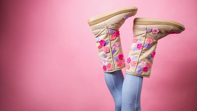 A pair of legs upside down, wearing skinny jeans and a pair of boots decorated with flowers - bright pink background.