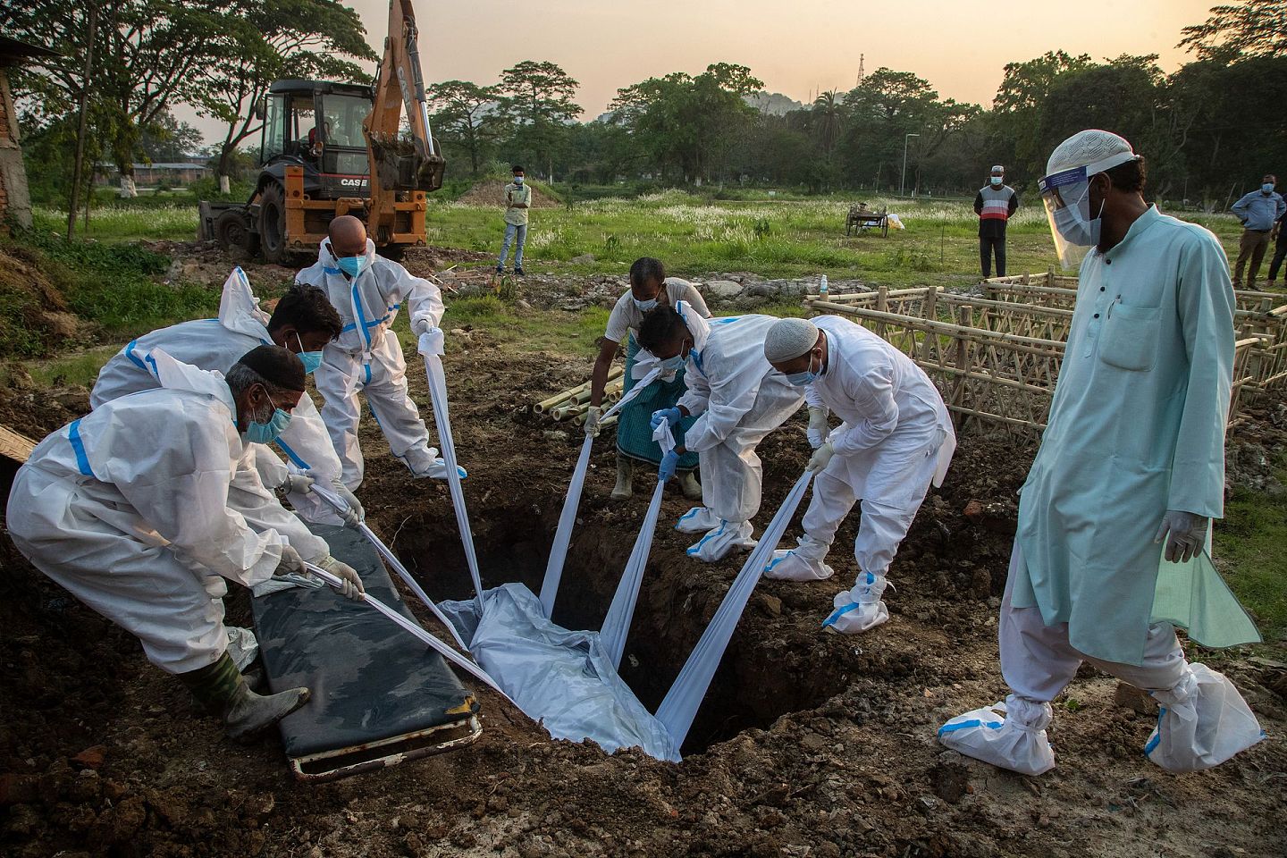 2021年4月25日，印度市政工作人员和死者家属穿着防护服，将死者尸体埋葬。（AP）