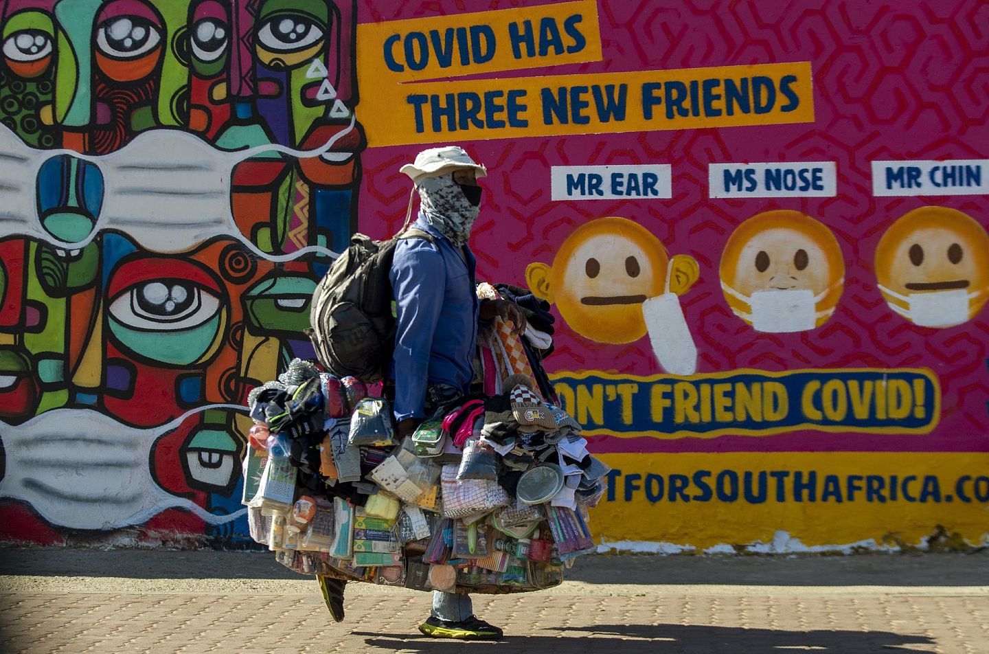 5月15日，南非索韦托，一个携带商品的街头小贩走过一幅关于如何戴上口罩以防止新冠肺炎传播的壁画。（AP）