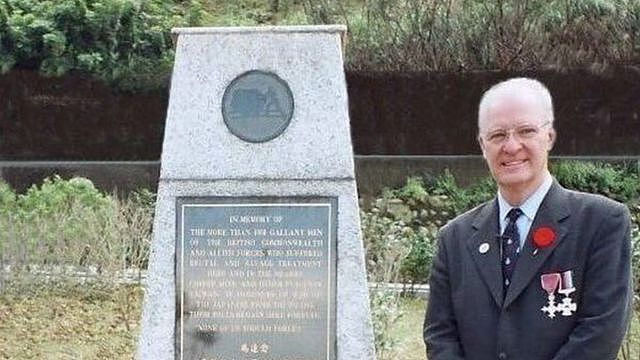 Michael Hurst standing in front of the memorial at the Kinkaseki memorial camp