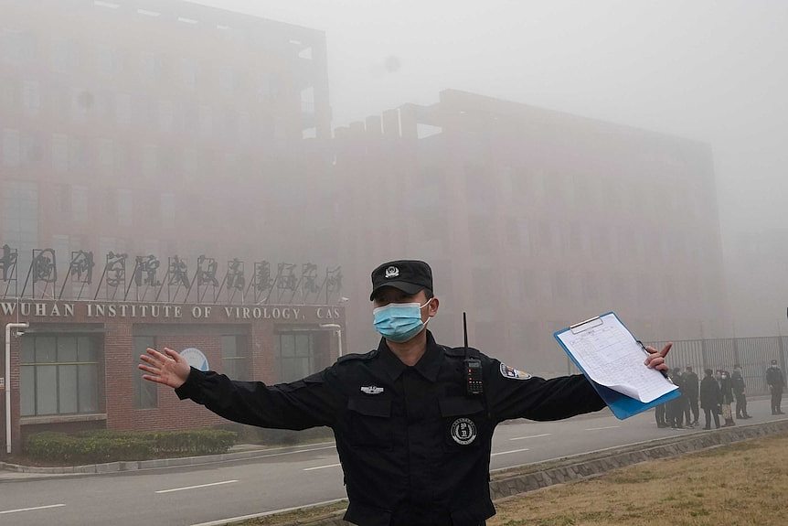 A security person moves journalists away from the Wuhan Institute of Virology