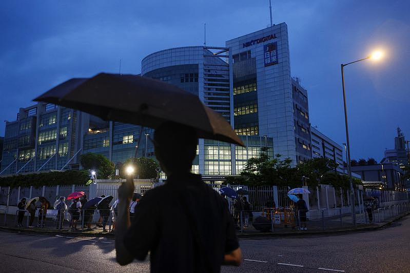 香港苹果日报24日出版最后一期报纸。 图为拿着伞的路人在夜幕中走过苹果日报大楼前，...
