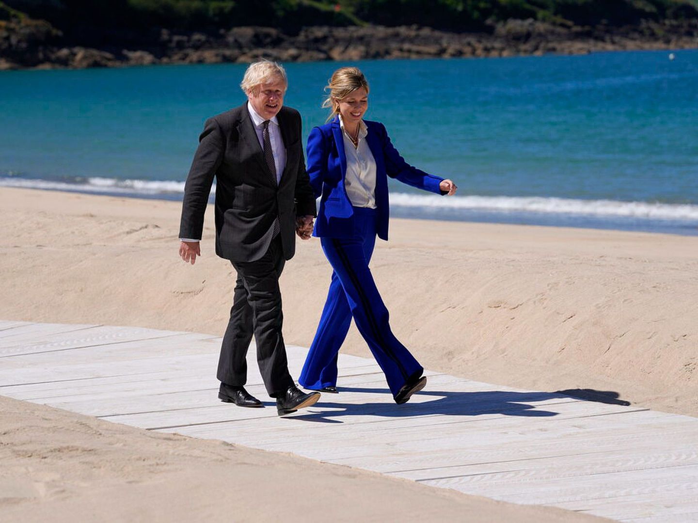 约翰逊夫妇从卡比斯海滩走过，凯莉身穿蓝色西装，内搭白衬衫，风格保守，但身材修长，胜过略微丰满的伊万卡。（AP）