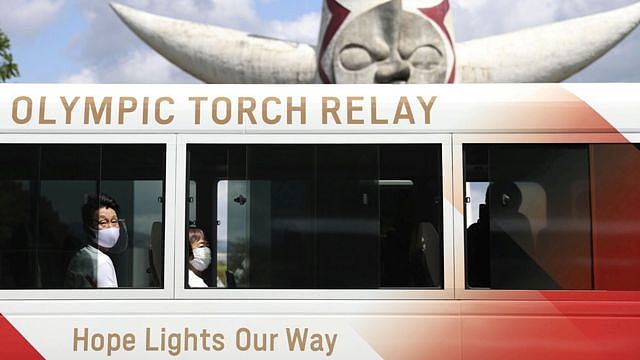 Tokyo 2020 Olympic Torch Relay runners wearing protective masks wait inside a bus for their run at the Expo 