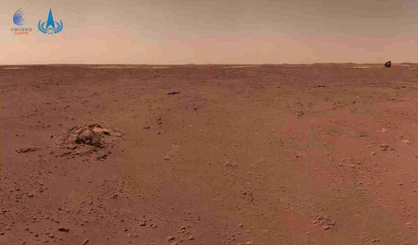 这是火星车拍摄的画面，图中左侧为一簇形状各异的石块，右上角可见背罩和降落伞，成像时火星车距离着陆点直线距离约210米，距离背罩和降落伞约130米。（微信@中国探月工程）