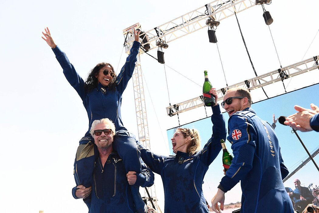 西丽莎·班德拉攀上布兰森的双肩庆祝，他们俩与贝丝·摩西（中）和科林·本内特（右）得到了赋予他们宇航员身份的翅膀胸针。