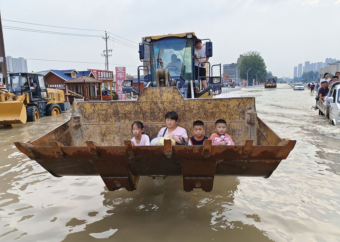 2021年7月22日，郑州，商都大道，宋女士带女儿和两个孙子坐铲车通过涉水路面。她打算回老家开封杞县。（人民视觉）