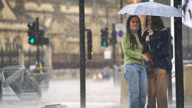 伦敦西敏寺议会广场上两位女士瑟缩在一把雨伞下（25/7/2021）