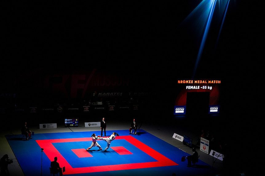 Two women compete in karate in the distance in a pool of light. 