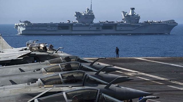 French navy Rafale jet fighters sit on the bridge of the French aircraft carrier Charles de Gaulle with the UK Royal Navy's aircraft carrier HMS Queen Elizabeth in the background during the Navy exercise 