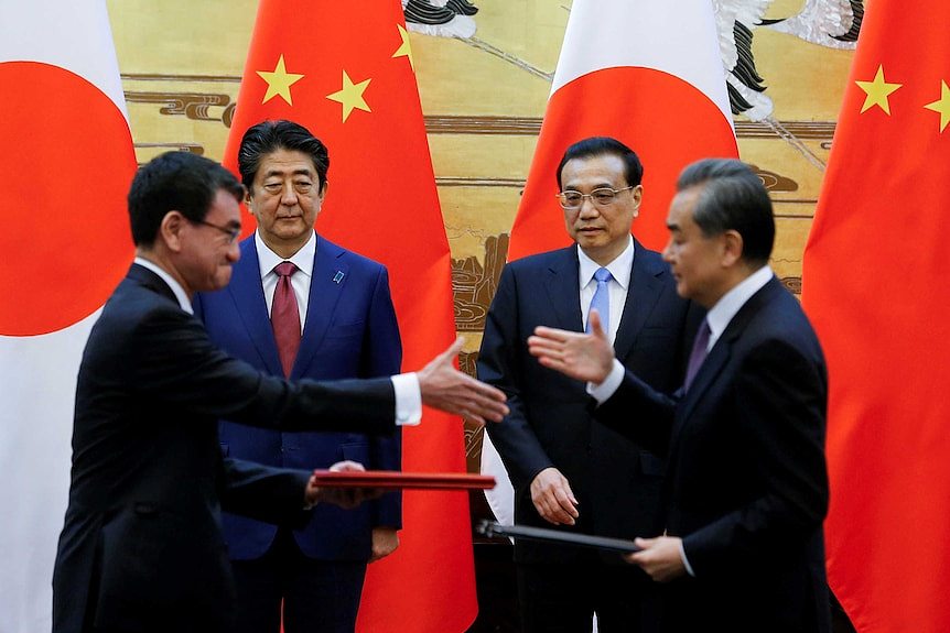Leaders of China and Japan shake hands while in front of large flags of their respective nations