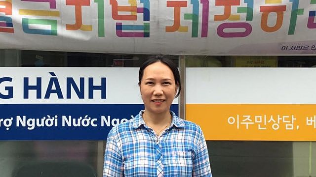 Won Ok Kum stands outside her office with Korean and Vietnamese signage on display.