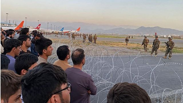 阿富汗人挤在机场附近的铁丝网后面注释着前面的美军士兵