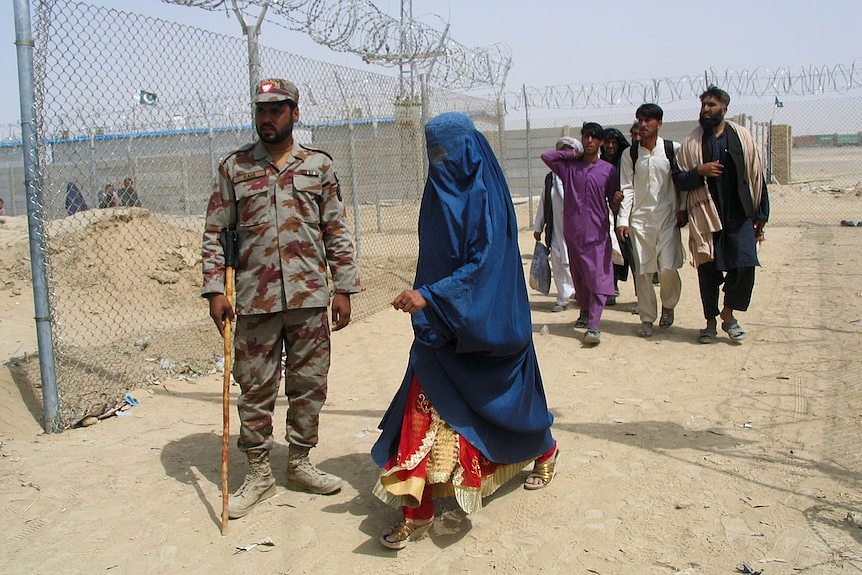 在边境检查站，一名身穿罩袍的阿富汗妇女从一名巴基斯坦准军事部队士兵身边走过
