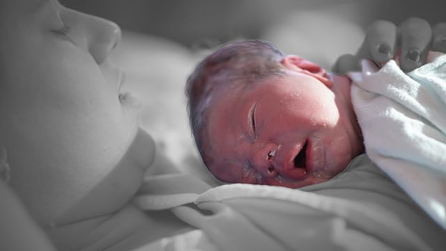 A woman holds a newborn who has a layer of vernix on his skin