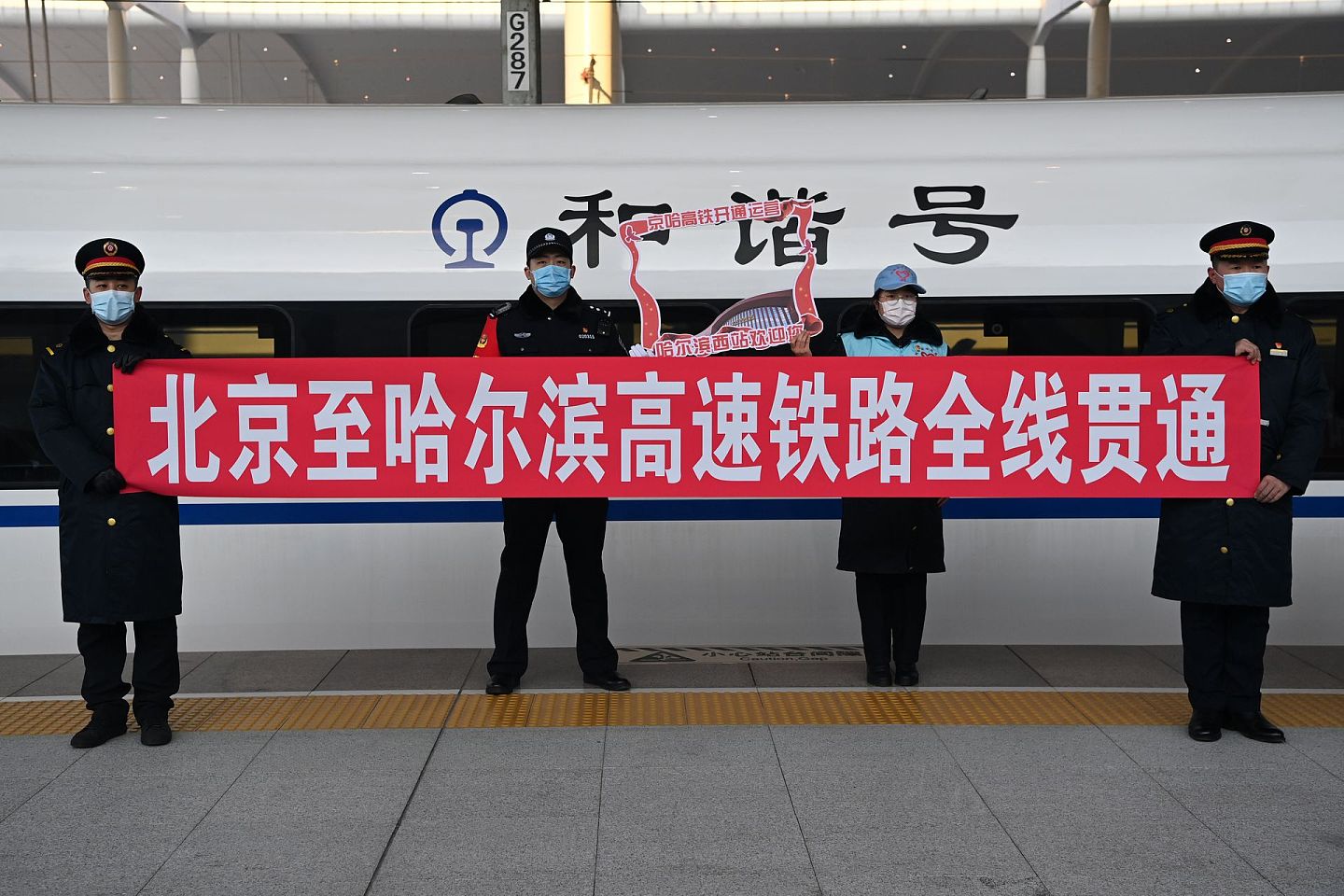 1月22日，在停靠于哈尔滨西站的京哈高铁G902次列车旁，工作人员和志愿者在留影。（新华社）