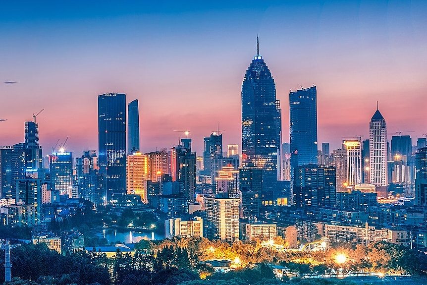 The skyline of Wuhan's Xibeihu area at dusk. There are skyscrapers and bright lights, and the sky is pink and blue.
