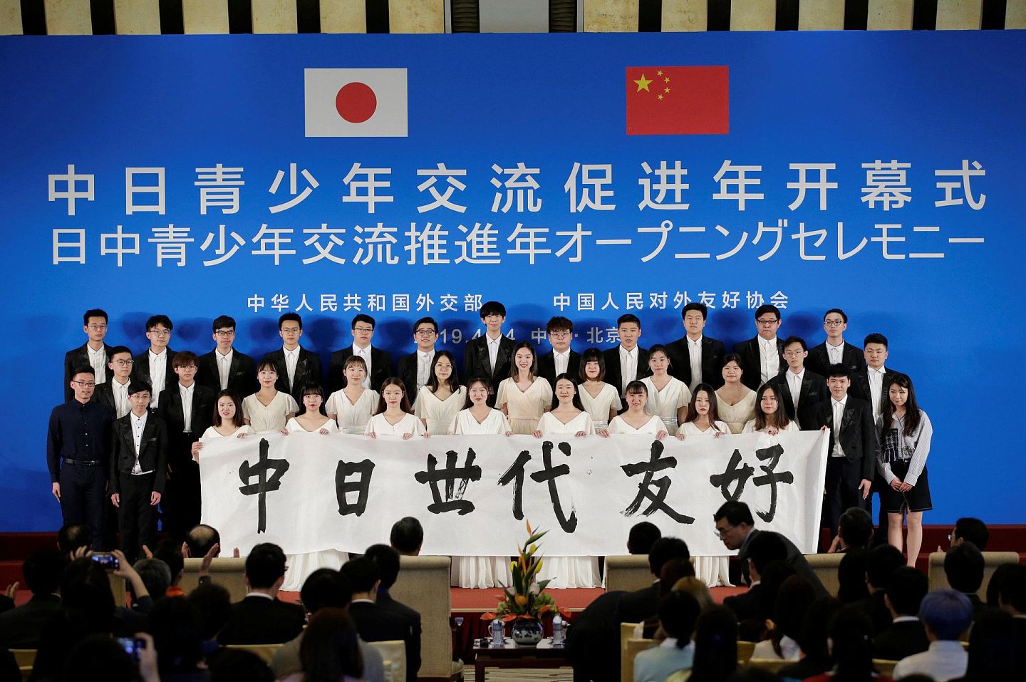 2019年4月14日，在北京钓鱼台国宾馆举行的中日青年交流年开幕式上，日本和中国女孩举着“中日友好世代相传”标语。（Reuters）