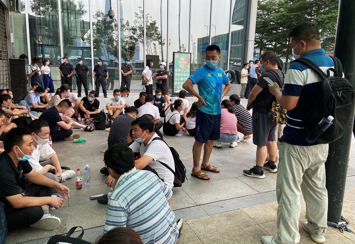 2021 年 9 月 16 日，中国广东省深圳市，人们坐在恒大总部旁边的地铁入口处，要求偿还贷款和金融产品，而保安人员在大楼外守卫。（Reuters）