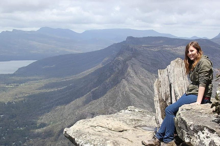 一位穿着套头衫的女性坐在山顶眺望远方