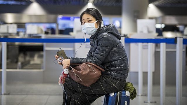 德国法兰克福机场一位中国女孩在值机柜台前坐在行李箱上等候（12/3/2021）