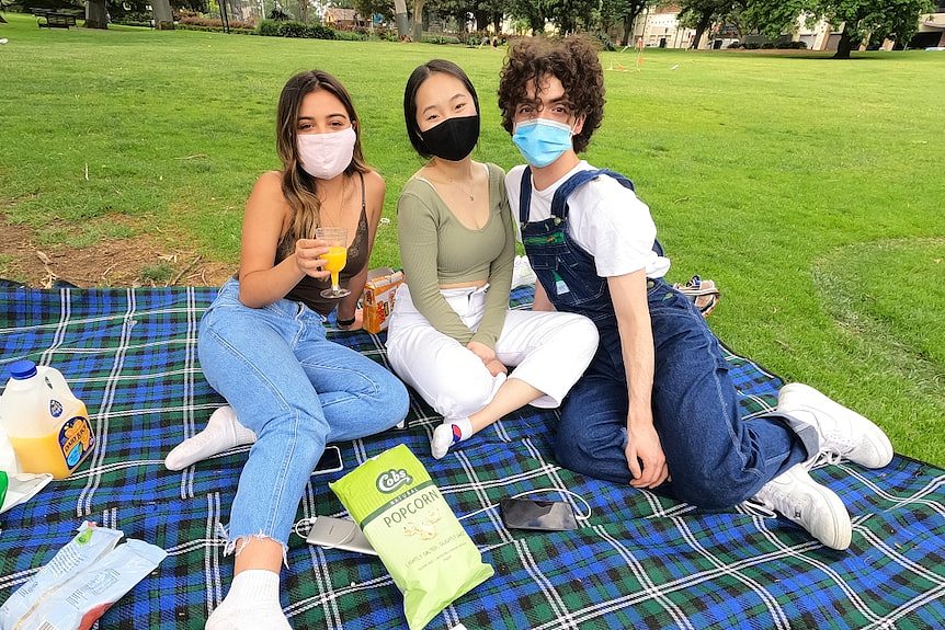 三个戴着口罩的人在公园野餐