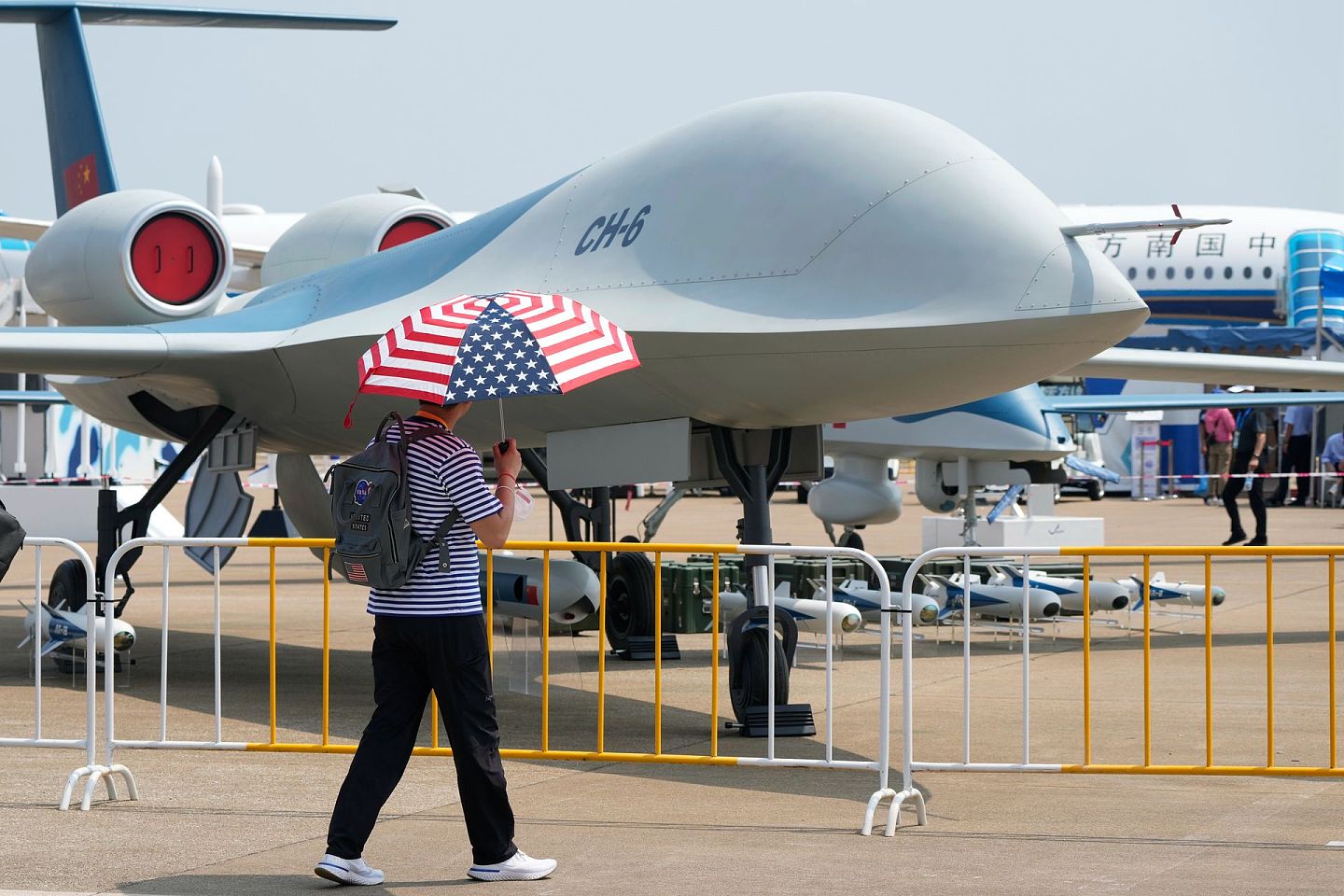 2021年9月28日，在广东省珠海举行的第13届中国国际航空航天博览会上，一名男子拿着一把印有美国国旗颜色的雨伞走过“彩虹-6”无人机。（AP）