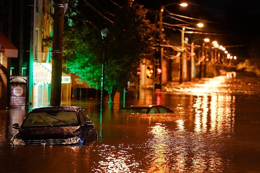 Cars sit submerged under deep floodwaters on a street at night