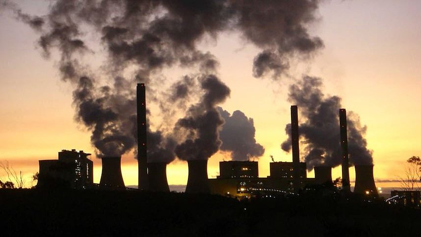 The silhouette of a smoking gas plant is contrasted against a golden sunset. 