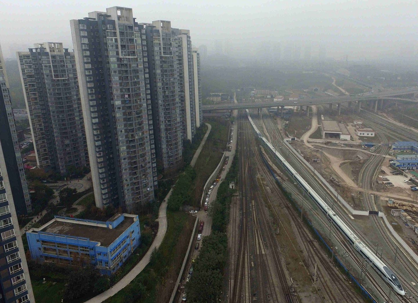 2015年12月26日，从重庆北站发出的成渝高铁重庆首发列车经过一片城市建筑。（新华社）