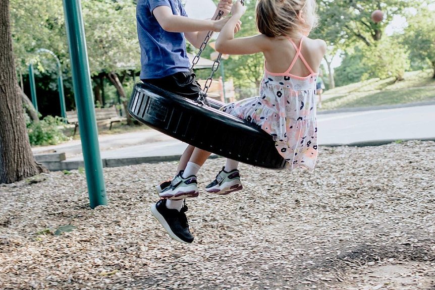 Two kids play on a swing.