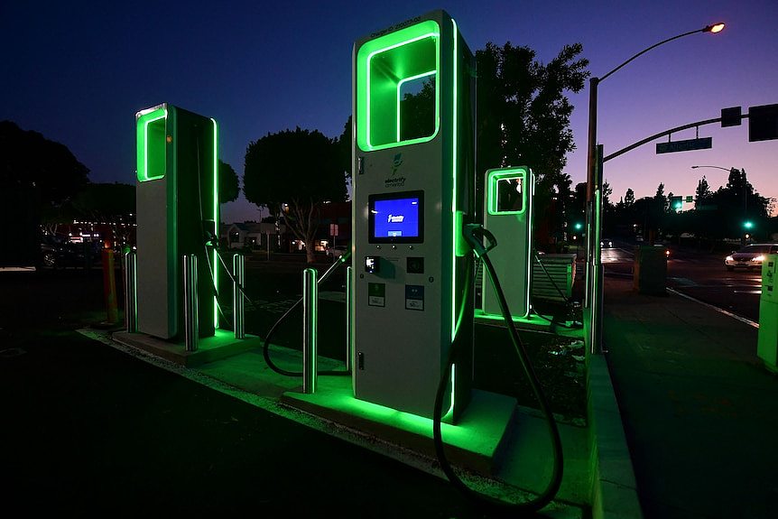 Green-glowing obelisks with charger cables by a roadside at night