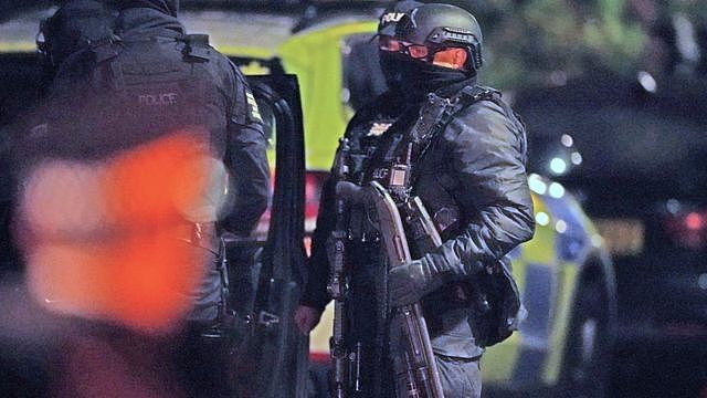 An armed police officer holds a breaching shotgun