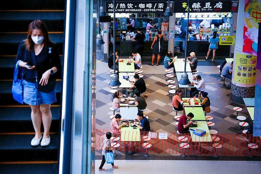 A woman goes down an escalator into a food court, where some seats are roped off 