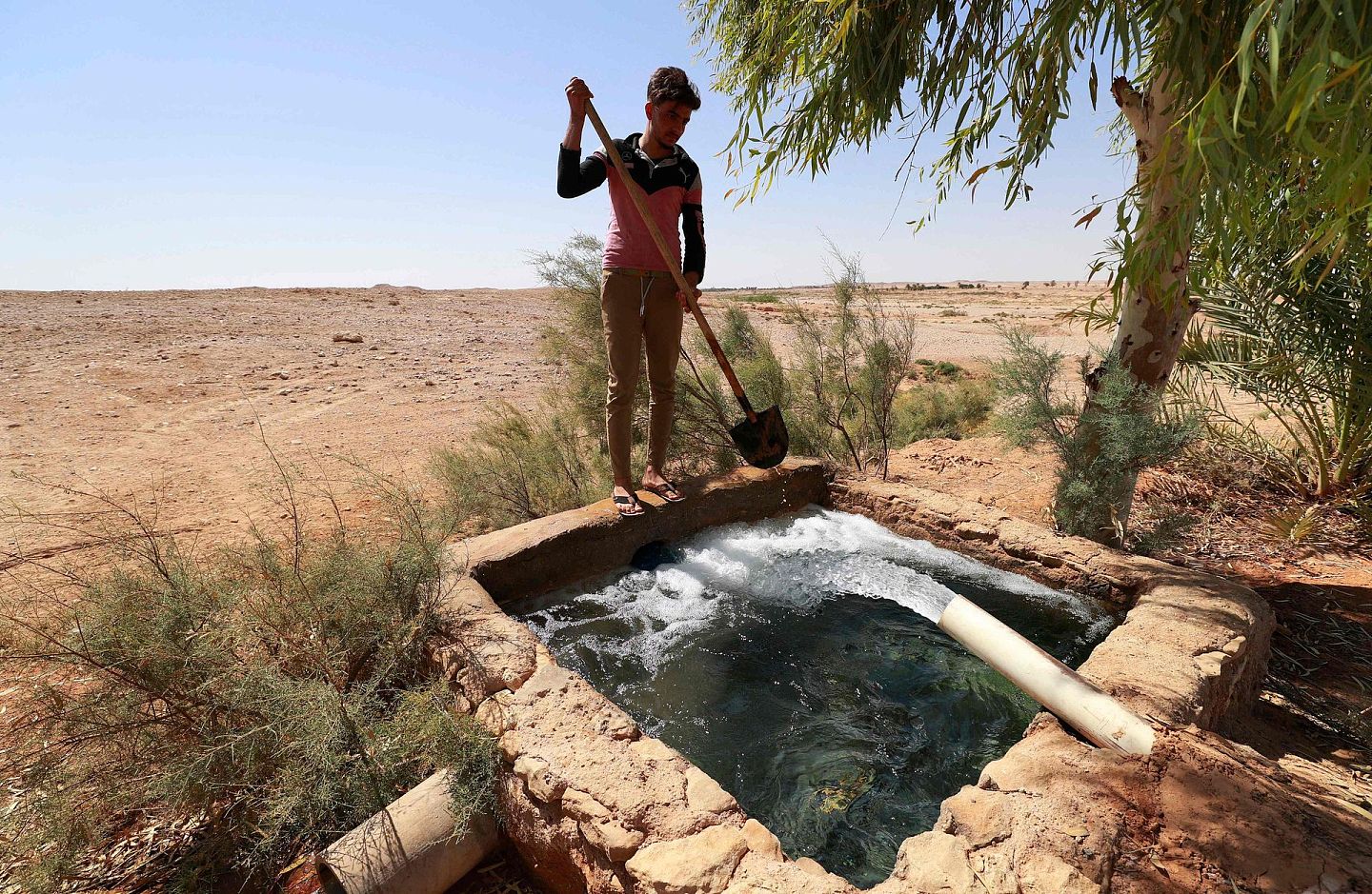 当地时间2021年9月16日，伊拉克安巴尔省中部Wadi Houran地区的Al-Sahl村，一位伊拉克农民在农田清洗他的铁锹。在伊拉克广阔的西部沙漠，大约有200户人家住在Al-Sahl村，一个与外界基本隔绝的小村庄，他们唯一的邻居是该国最大的军事基地之一。（视觉中国）