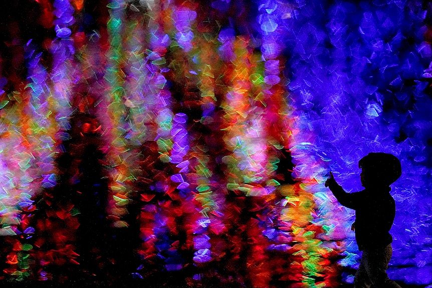 A boy is silhouetted against Christmas lights reflected on a pond as he walks through a park 