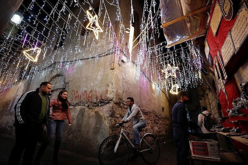 people walk in a street decorated with stars and lights in Syria