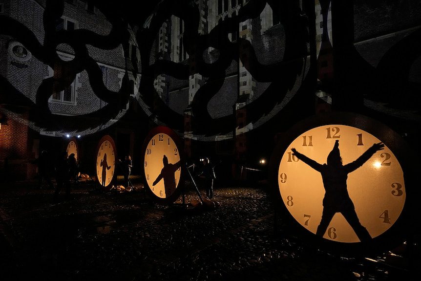 peoples' silhouettes can be seen in lit up clock faces near a building in Hampton Court Palace