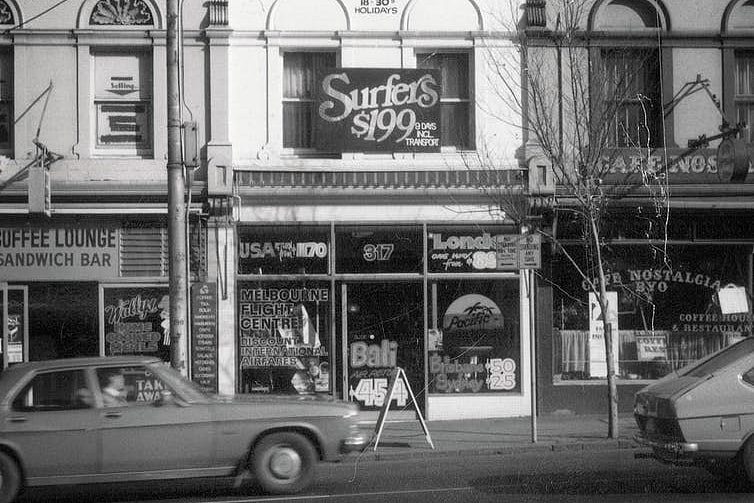 A black and white photo of a travel agent shopfront advertising Bali and Surfers