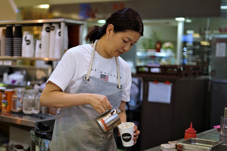 A woman in an apron makes a coffee.