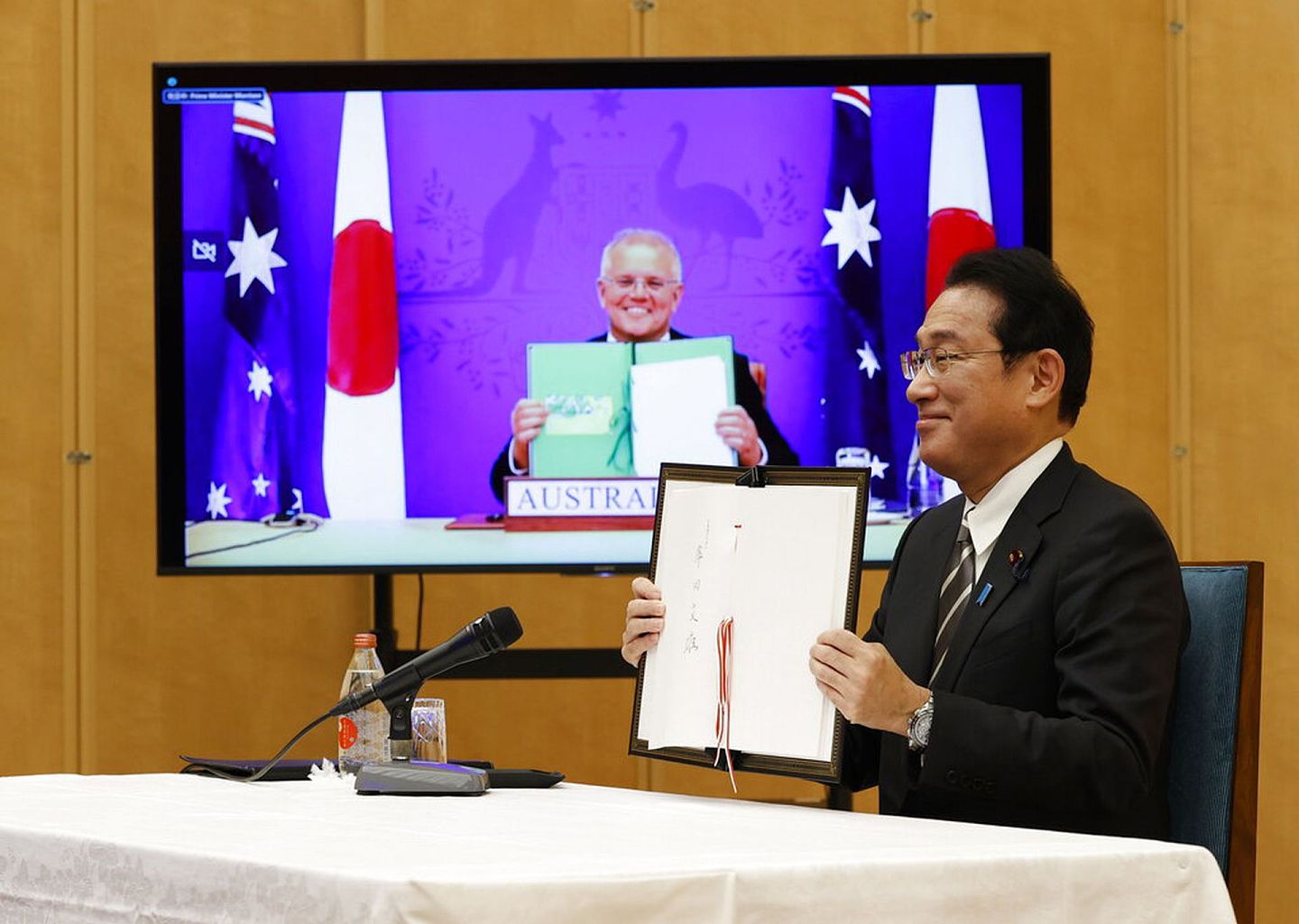 2022年1月6日，日本首相岸田文雄（右）和澳大利亚总理莫里森（左）在视频会晤上展示已经签署的日澳《互惠准入协定》的文件。（AP）